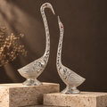 Ornate silver swan pair displayed on travertine plinths