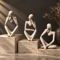 Three cream resin thinker sculptures on travertine plinths